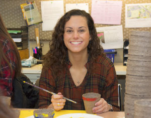 Madison Dox paints pottery in volunteer workroom on her 18th birthday.